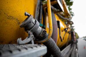 Side view of powerful professional modern yellow sewage sewerage truck working near a house pumping basement canalisation water.