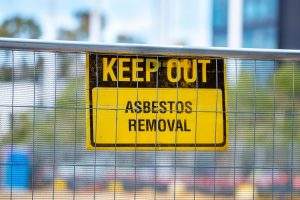 KEEP OUT ASBESTOS REMOVAL warning sign on a construction fence. This image represents our specialized hazardous waste management, asbestos abatement, and environmental remediation services, ensuring safe and compliant removal of dangerous materials.